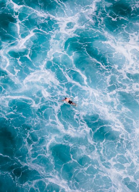 High-angle view of a lone swimmer amidst vibrant blue ocean waves.