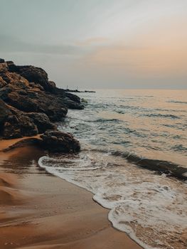 Peaceful coastal view of Ténès Beach in Algeria during a stunning sunset with waves and rocky formations.
