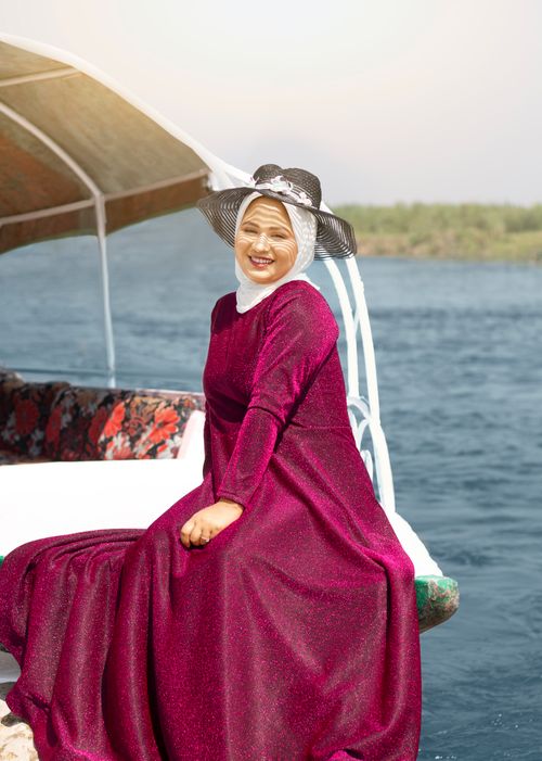 Free A smiling woman in a bright magenta dress sits on a boat, enjoying a sunny summer day. Stock Photo