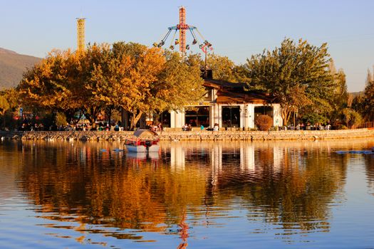 Charming autumn scene featuring an amusement park by a tranquil lake at sunset. Reflections and golden hues create a peaceful atmosphere.