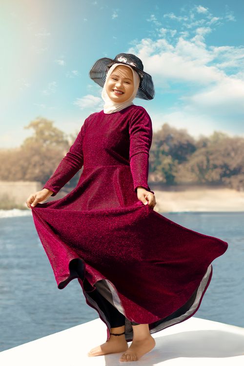 Free A joyful woman in a red dress enjoys a sunny day by the calm sea, showcasing elegance and happiness. Stock Photo