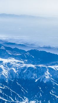 A breathtaking aerial view of snow-capped mountains surrounded by mist and fog.