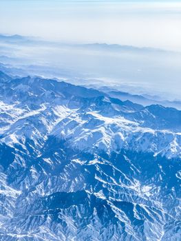 Breathtaking aerial shot of snow-covered mountain peaks under a clear sky, highlighting natural beauty.