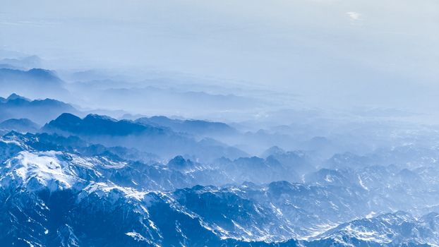A stunning aerial view of snow-capped mountains enveloped in mist and fog.