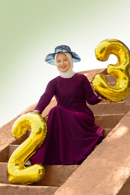 Free A woman in a purple dress and hat holds golden balloons celebrating her 23rd birthday outdoors. Stock Photo