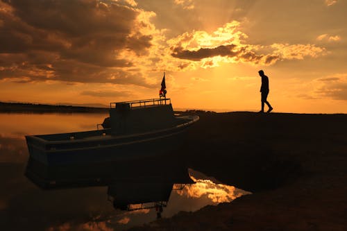 Silhouette of Person Walking near the Boat 