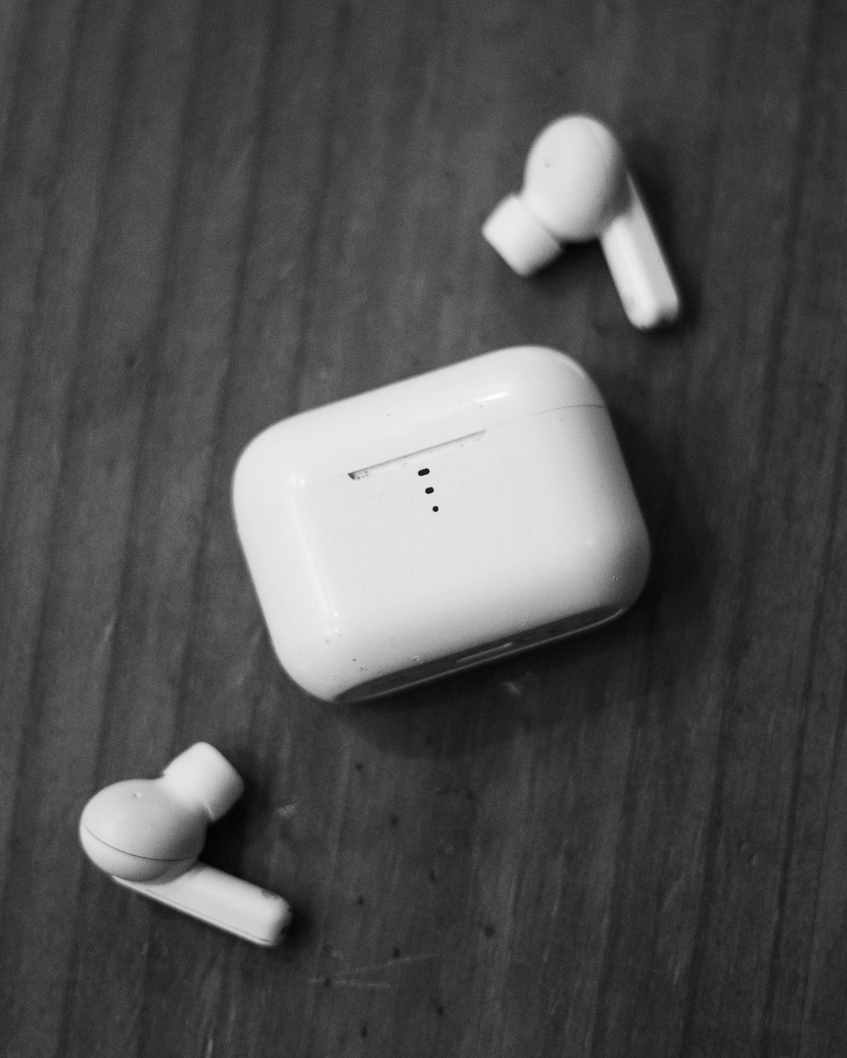 Grayscale close-up of a single wireless earbud on a wooden surface
