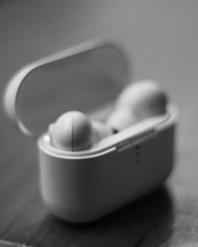 Black and white close-up of wireless earbuds in a charging case on a table.