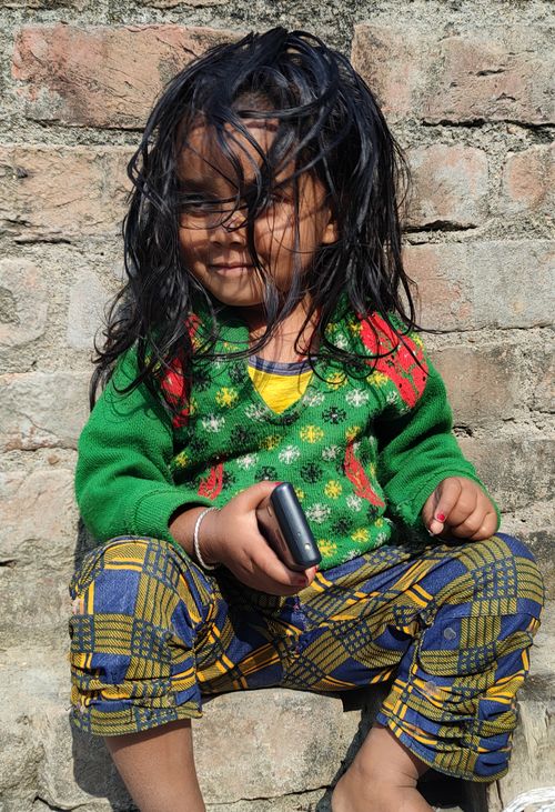Free Smiling young girl in colorful outfit sitting against a brick wall in Bihar, India. Stock Photo