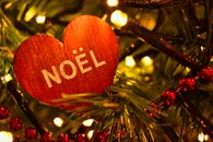 Close-up of a heart-shaped Noël ornament on a Christmas tree with glowing lights.