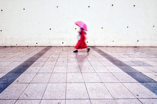 Free Blurred motion of a woman with an umbrella walking along a city pavement, creating a dynamic urban scene. Stock Photo