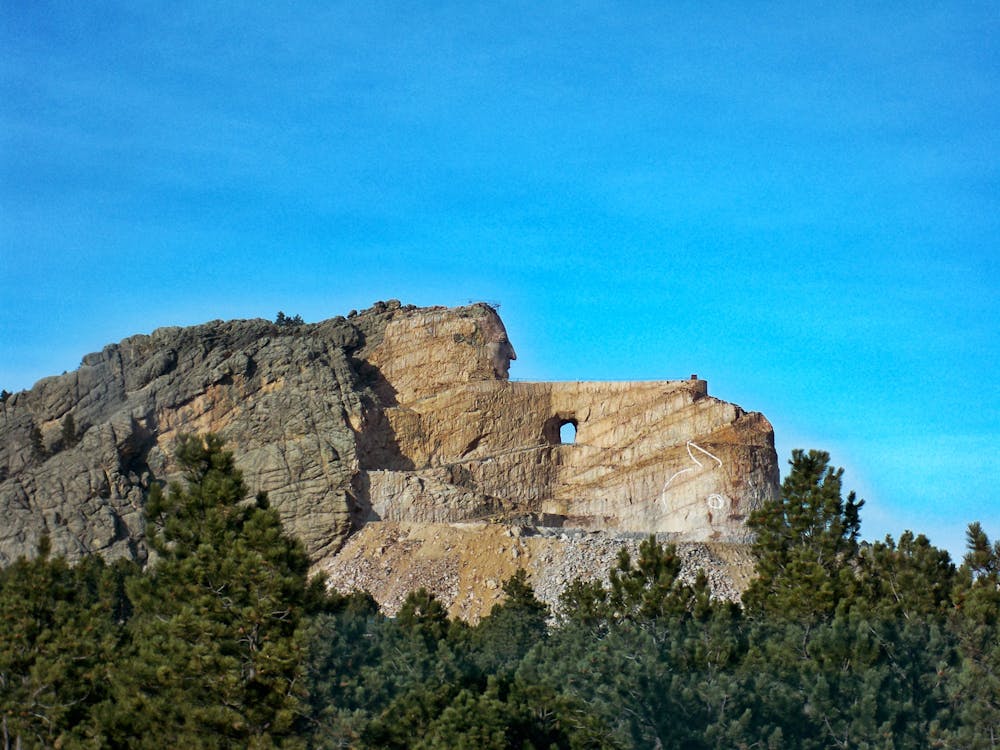 無料 昼間の澄んだ青い空の下でベージュと灰色の山の横にある緑の木 写真素材