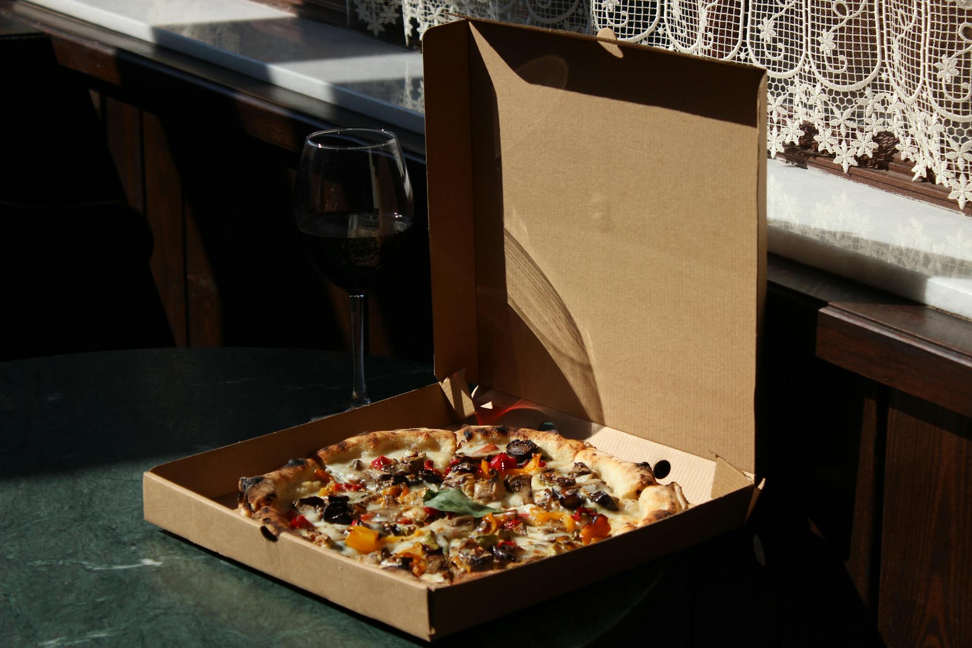 Pizza inside a Box Beside a Glass of Wine