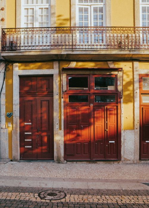 Free Yellow facade with wooden doors and balcony in Portas, Portugal captures architectural charm. Stock Photo