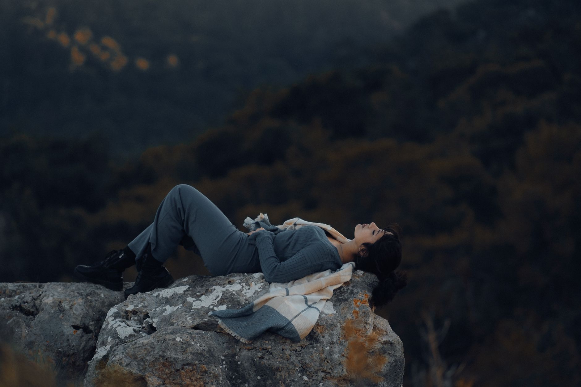 A woman in outdoor attire peacefully rests on a large rock in a natural setting. Adventure and tranquility blend harmoniously.