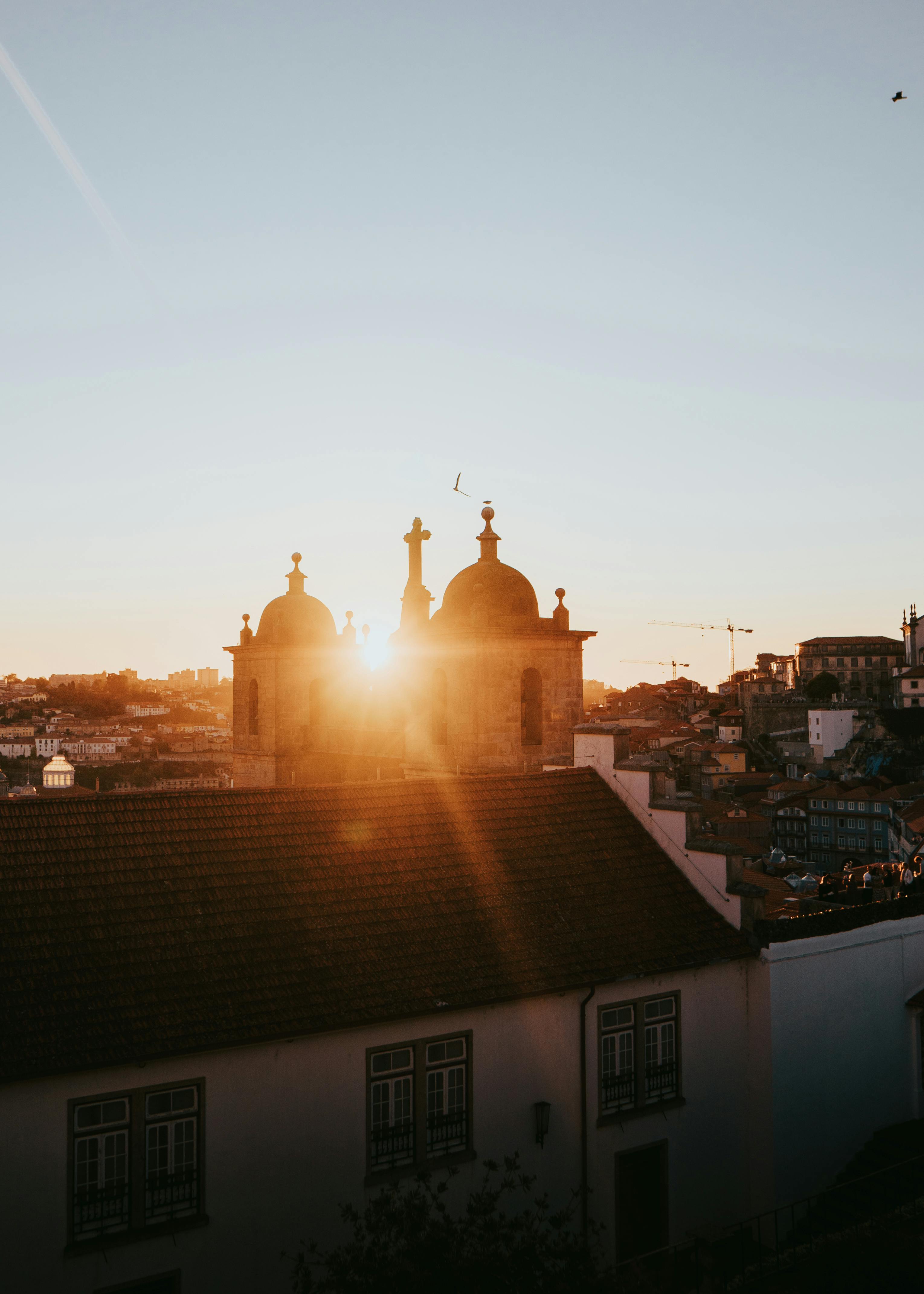 Sunlight beams over Porto's historic church towers at sunrise, capturing the city's charm.