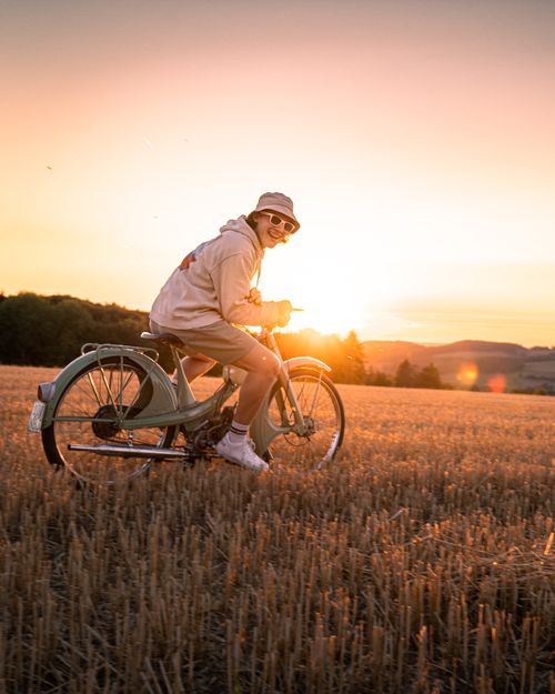 Free A man in bucket hat smiles while biking through a field at golden hour. Perfect for lifestyle and travel themes. Stock Photo