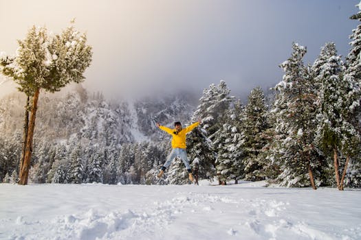 A person wearing a yellow jacket joyfully jumps in a snowy forest setting during winter.