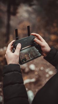 A close-up of hands operating a drone controller with a smartphone in the forest.