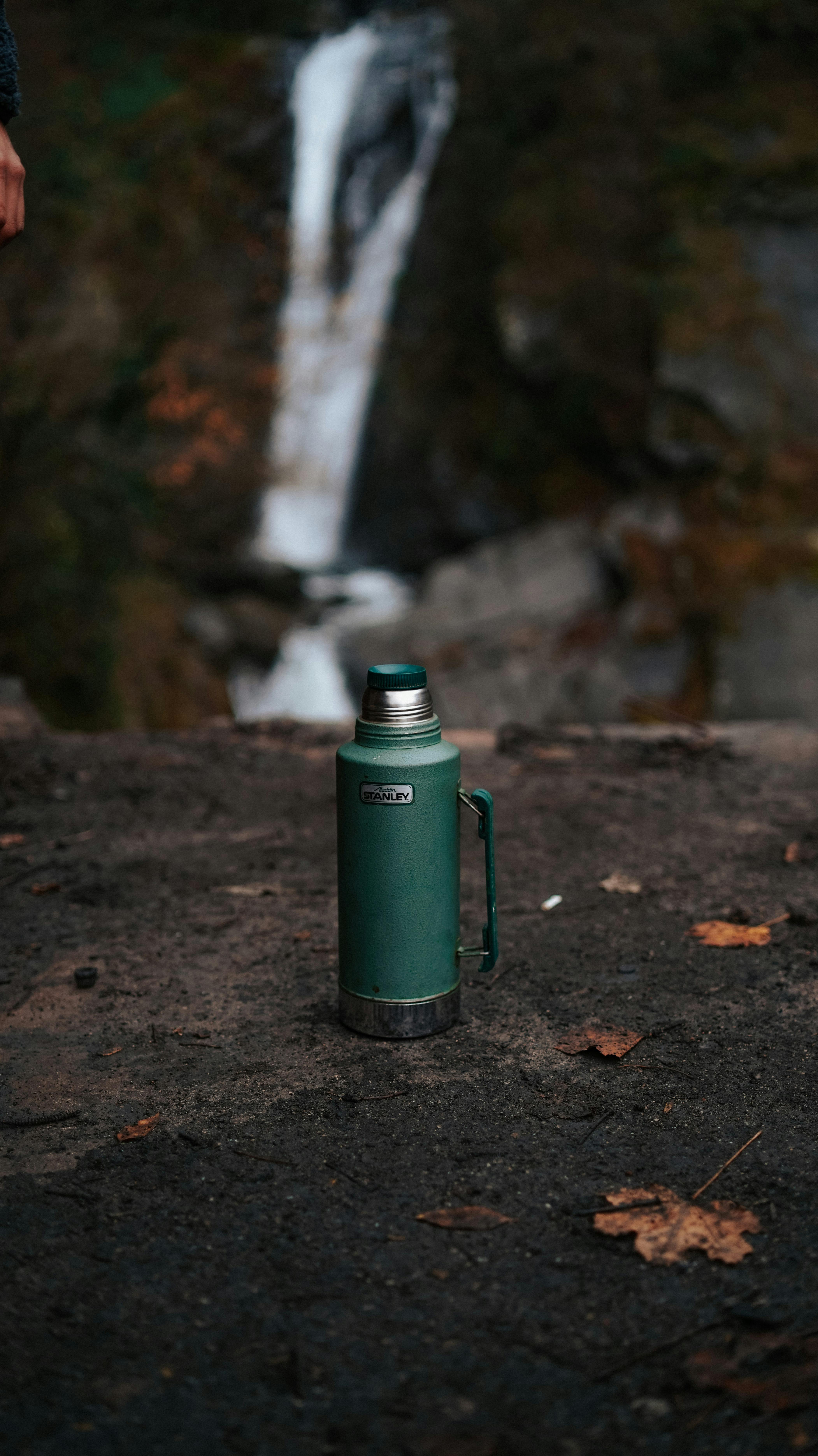 Thermos with a hot drink on mountain waterfall Stock Photo by