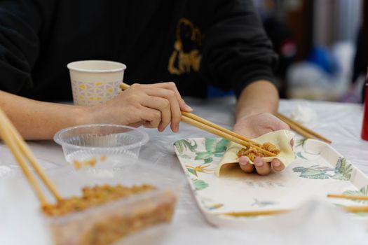 Close-up of hands using chopsticks to prepare Asian food on a table.