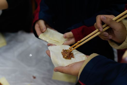 Close-up of hands preparing dumplings using chopsticks, showcasing traditional Asian cuisine.