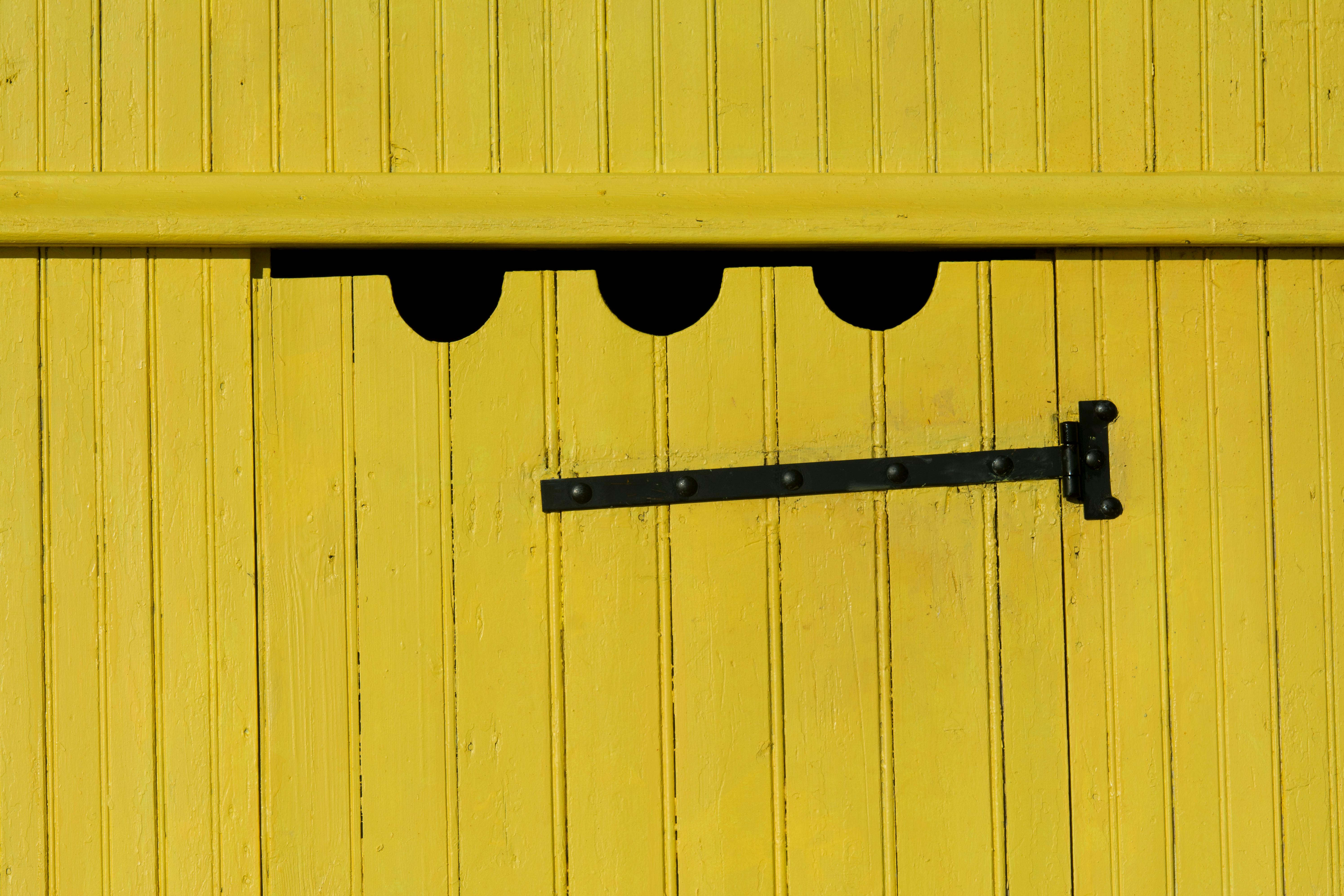 customizable barn door hardware designs - Close-up of a bright yellow wooden barn door with a black hinge, showcasing rustic rural charm.