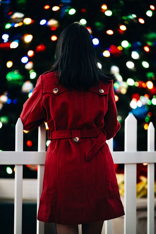 Free Back view of a woman in a red coat standing by a holiday lights display. Stock Photo
