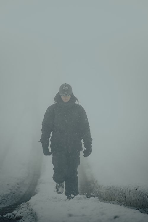 Free A person in winter clothing walks through a snow-covered path in a foggy setting. Stock Photo