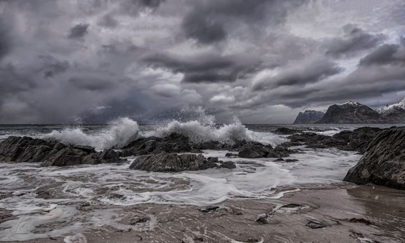 Breathtaking view of waves crashing on rocks under stormy skies in Myrland, Norway.