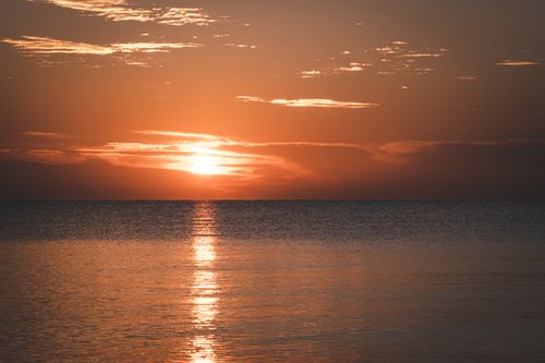Free Tranquil ocean sunset with golden reflections and dramatic clouds. Stock Photo