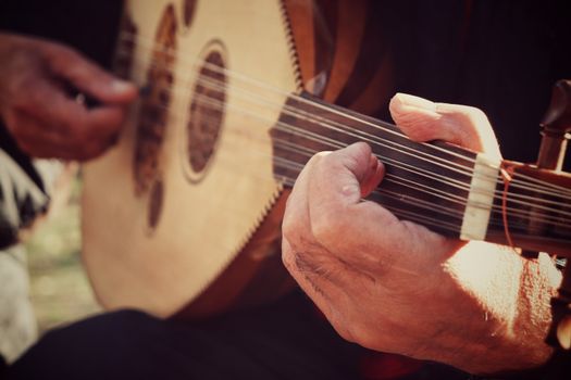 Detailed close-up of hands playing an oud, highlighting the strings and craftsmanship of the instrument.