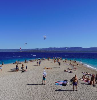 A lively summer day on a scenic beach with people relaxing and kite surfers catching the breeze.