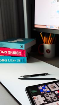 Modern workspace featuring design books, tablet, pen, and computer monitor, ideal for creative professionals.