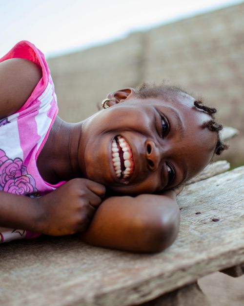Free Happy young girl smiling and lying on a wooden bench outdoors, capturing pure joy. Stock Photo