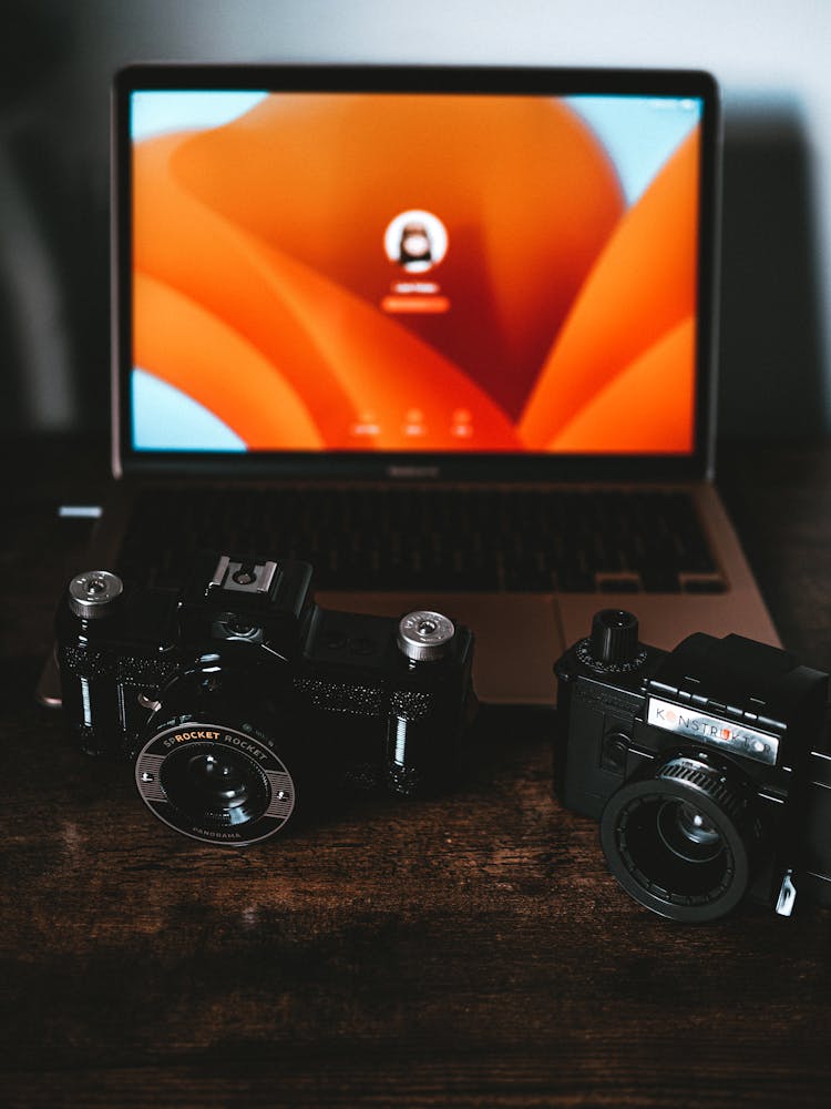 Two Cameras And A Laptop On A Desk