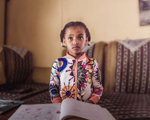 Free A young girl in a colorful outfit studying indoors, focused on her book. Stock Photo