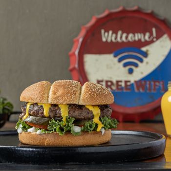A close-up of a delicious cheeseburger with toppings on a plate beside a retro sign.