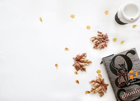 白色背景上，书和咖啡杯平放着，四周散落着秋叶