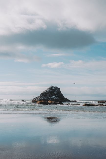 Tranquil scene of a rocky beach under dramatic clouds with clear reflections.