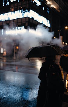 Silhouette of a person holding an umbrella on a rainy city street at night.