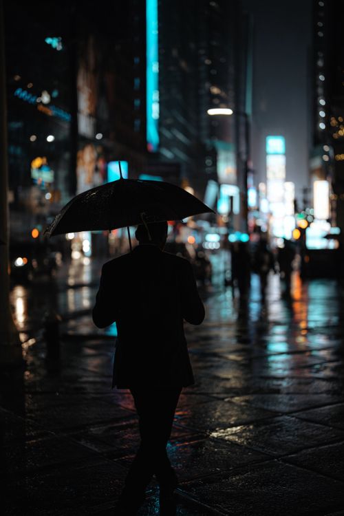 Free A person with an umbrella walks through a rainy, illuminated urban nightscape, reflecting city lights. Stock Photo