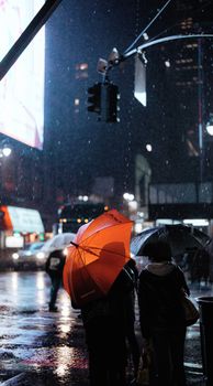 Urban street scene with people under umbrellas during rain at night.