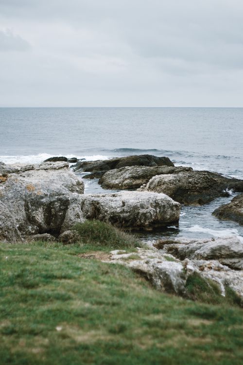 Free A tranquil view of a rocky shoreline against a calm sea under an overcast sky. Stock Photo