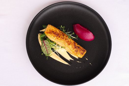 Top view of a gourmet salmon dish with colorful sauces on a dark plate.