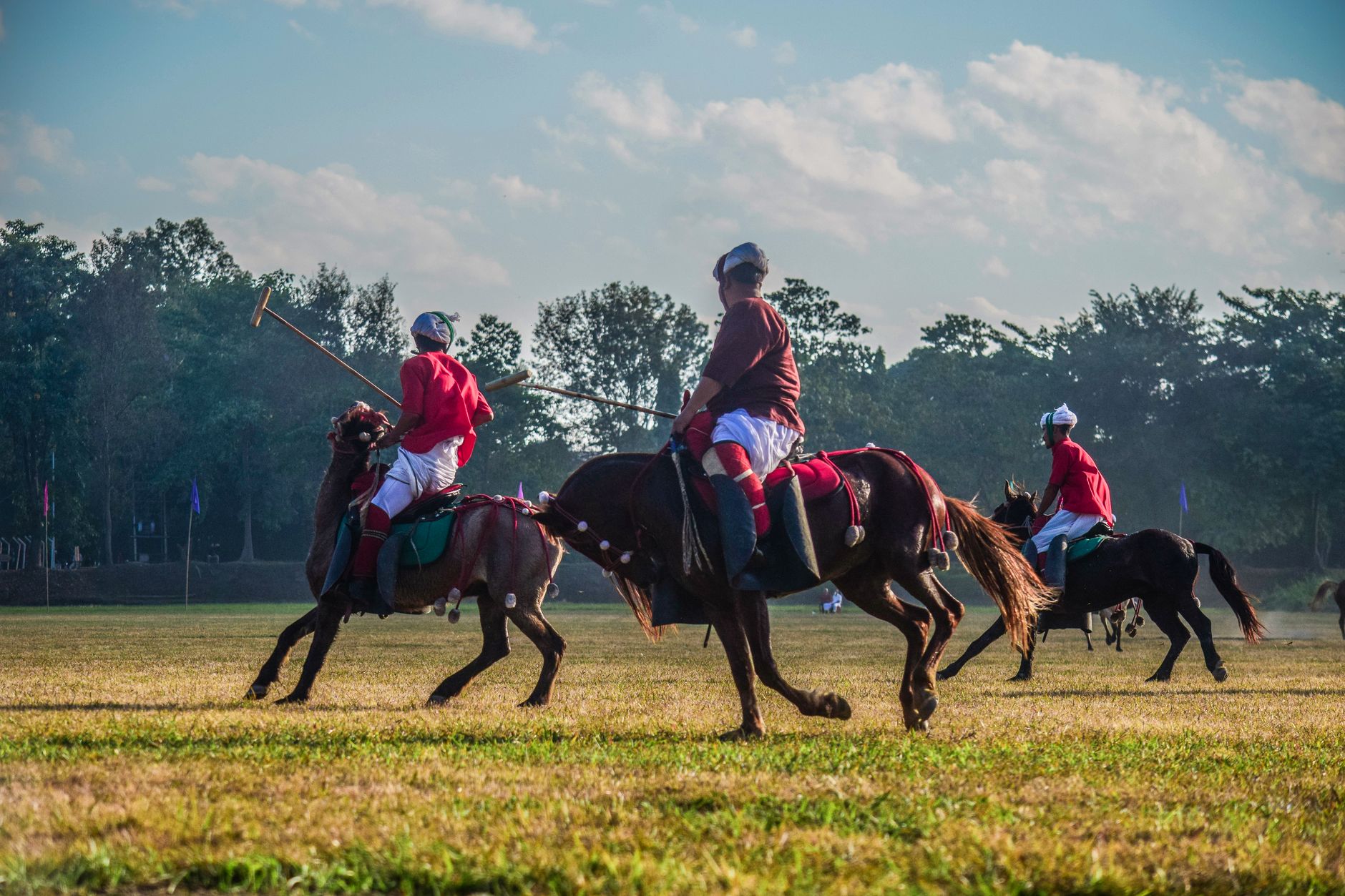 Action-packed polo match with players in red uniforms on horses in sunny Imphal, MN, India.