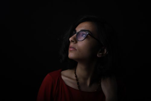 Free Dramatic studio shot of a woman with glasses looking upwards against a black background. Stock Photo