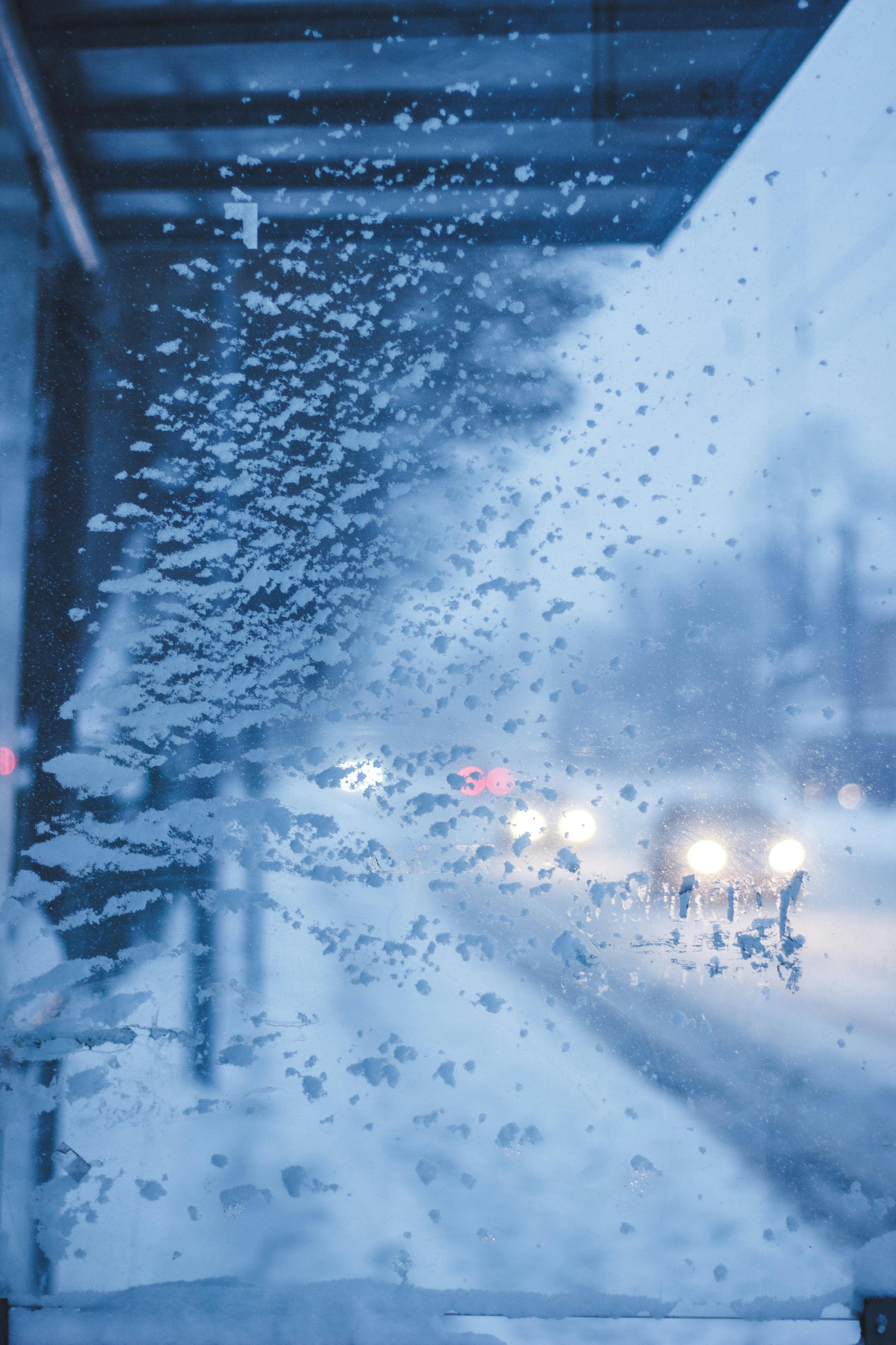 Icy bus stop window with snow and blurred headlights in the winter season.
