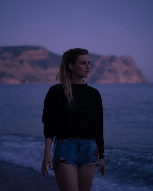 Free A young woman strolls along the beach at dusk, with cliffs in the background. Stock Photo