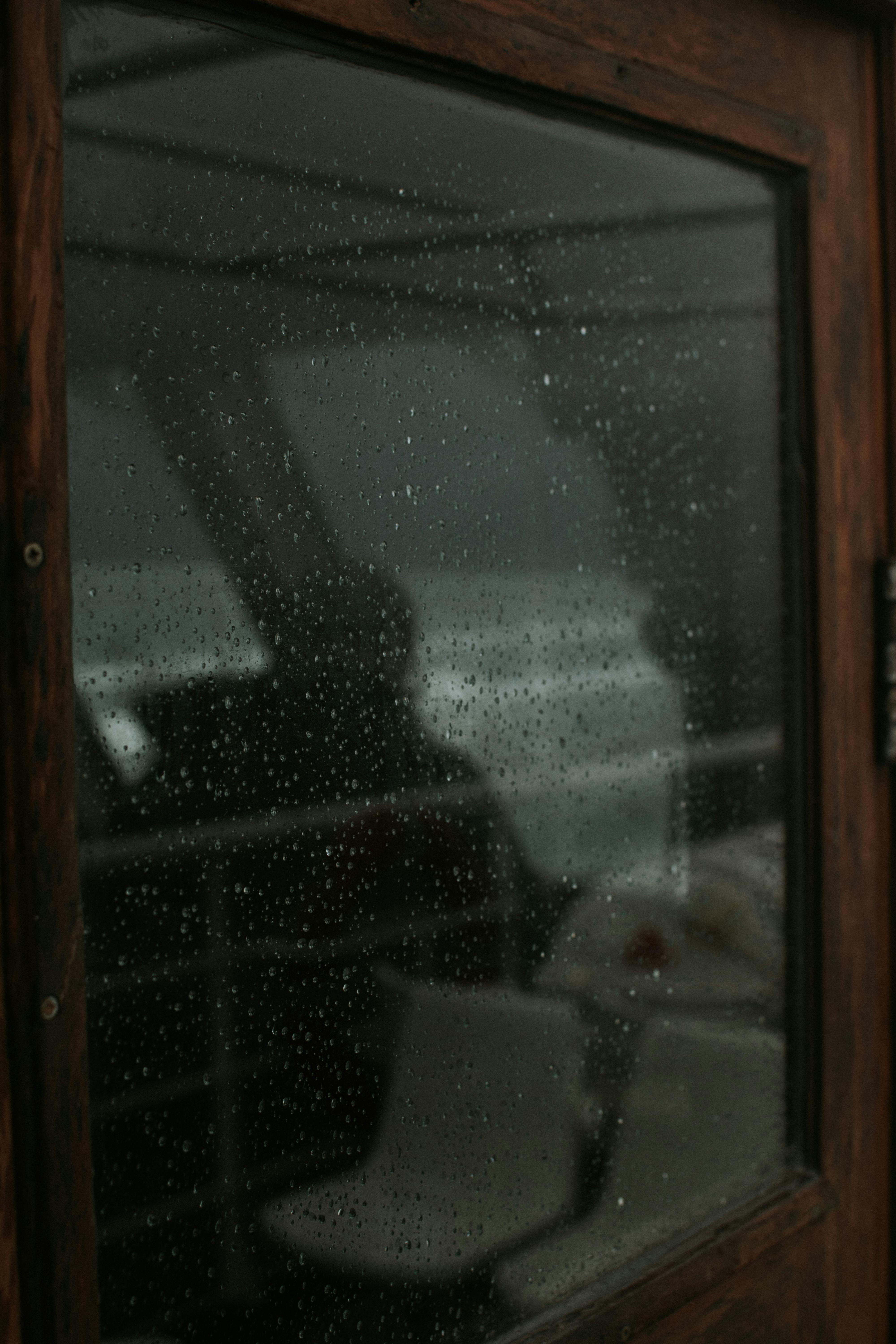 Close-up of raindrops on a window with an outdoor view, creating a moody atmosphere.